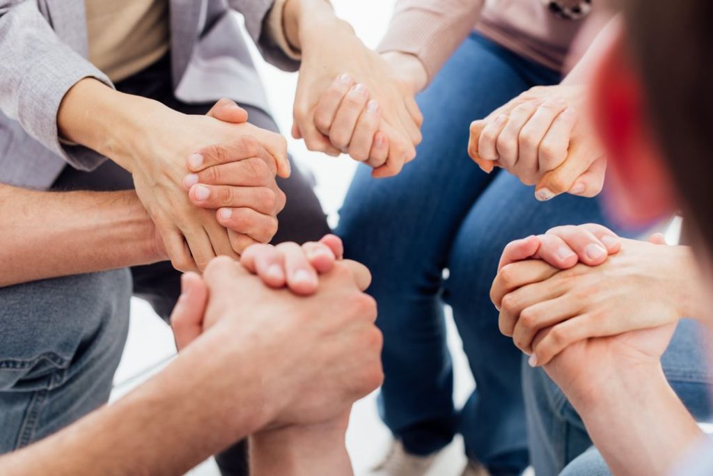 A group of people holding hands to heal a meth addict.