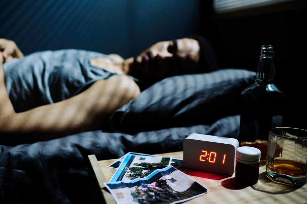 a soldier in bed with pills and alcohol on his nightstand. This man is suffering from substance abuse in the military