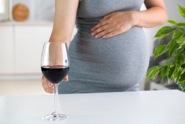 A pregnant woman reaching for a glass of wine, raising the chances that her baby will be born with NAS
