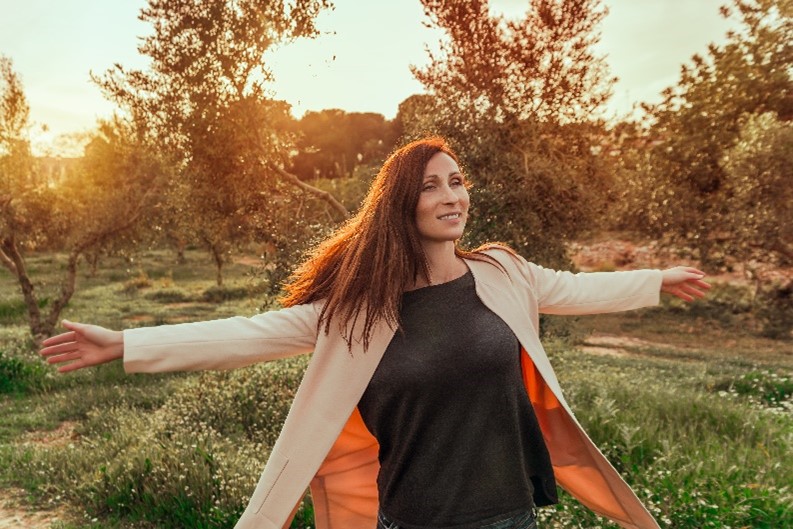 a woman spreading her arms with joy in a field after deciding between cognitive behavioral therapy vs psychotherapy for addiction