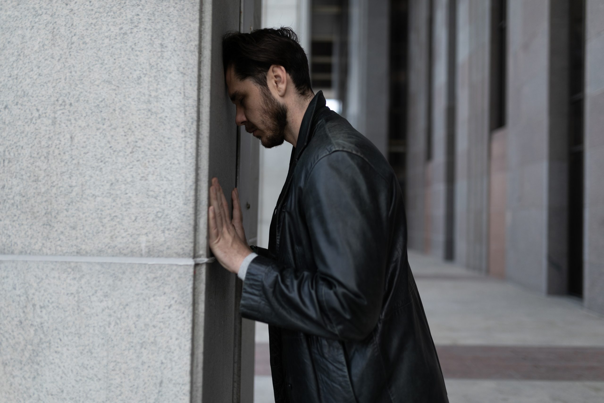 a young man with his head against a wall, wondering if drug relapse is a sign of treatment failure