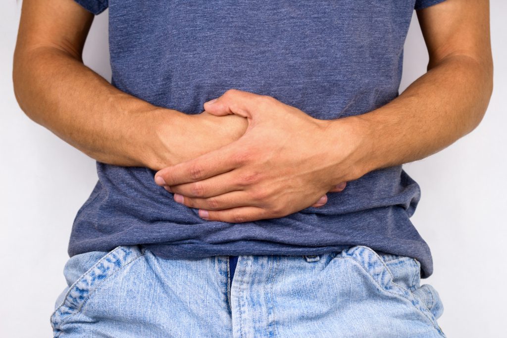 a man in pain holding his abdomen, a sign of coke bloat