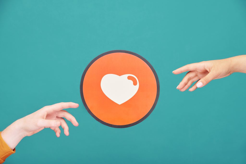 Two hands outstretched towards a heart in a red circle symbolizing caregiver vs caretaker in addiction roles