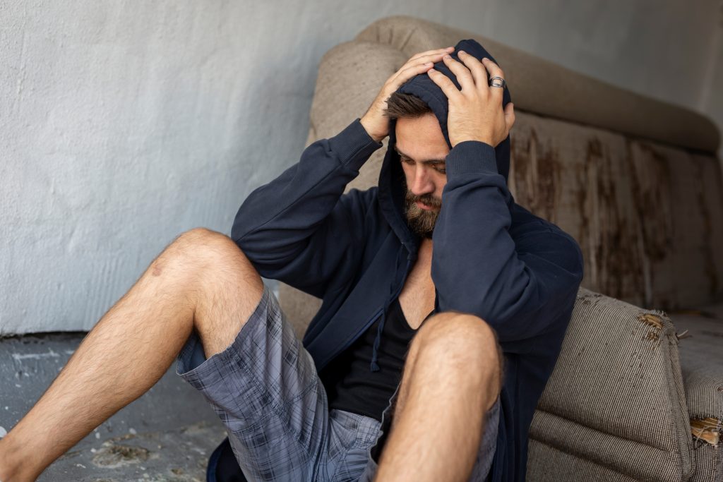 A depressed man siting against his couch with hands on his head, highlighting the problem of men and substance abuse