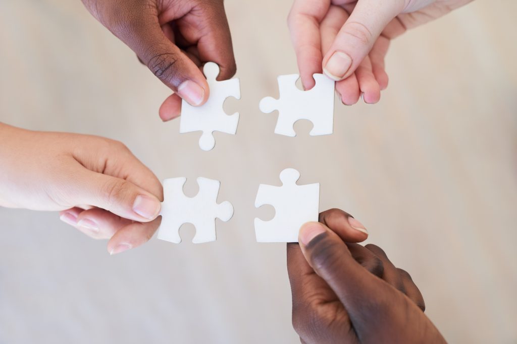 four hands holding puzzle pieces, showing we need unity to break the stigma of addiction