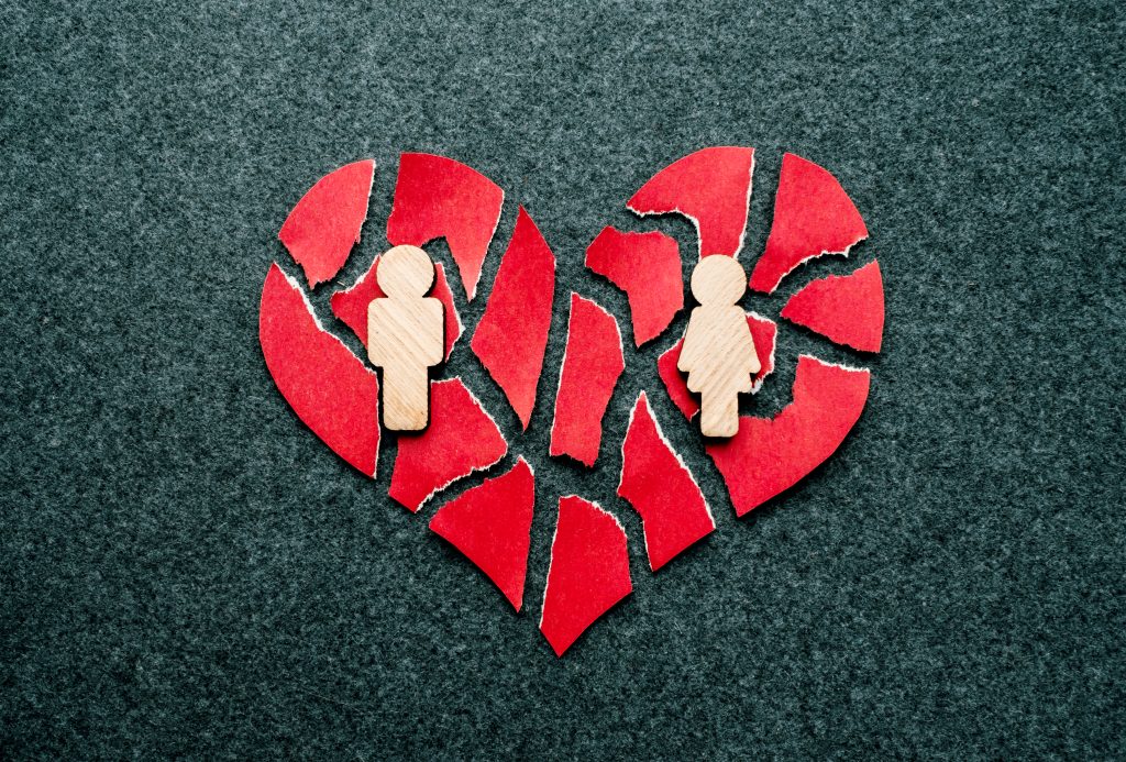 paper broken heart with wooden figures of a man and a woman on a dark background highlighting how shattering addiction and relationships can be
