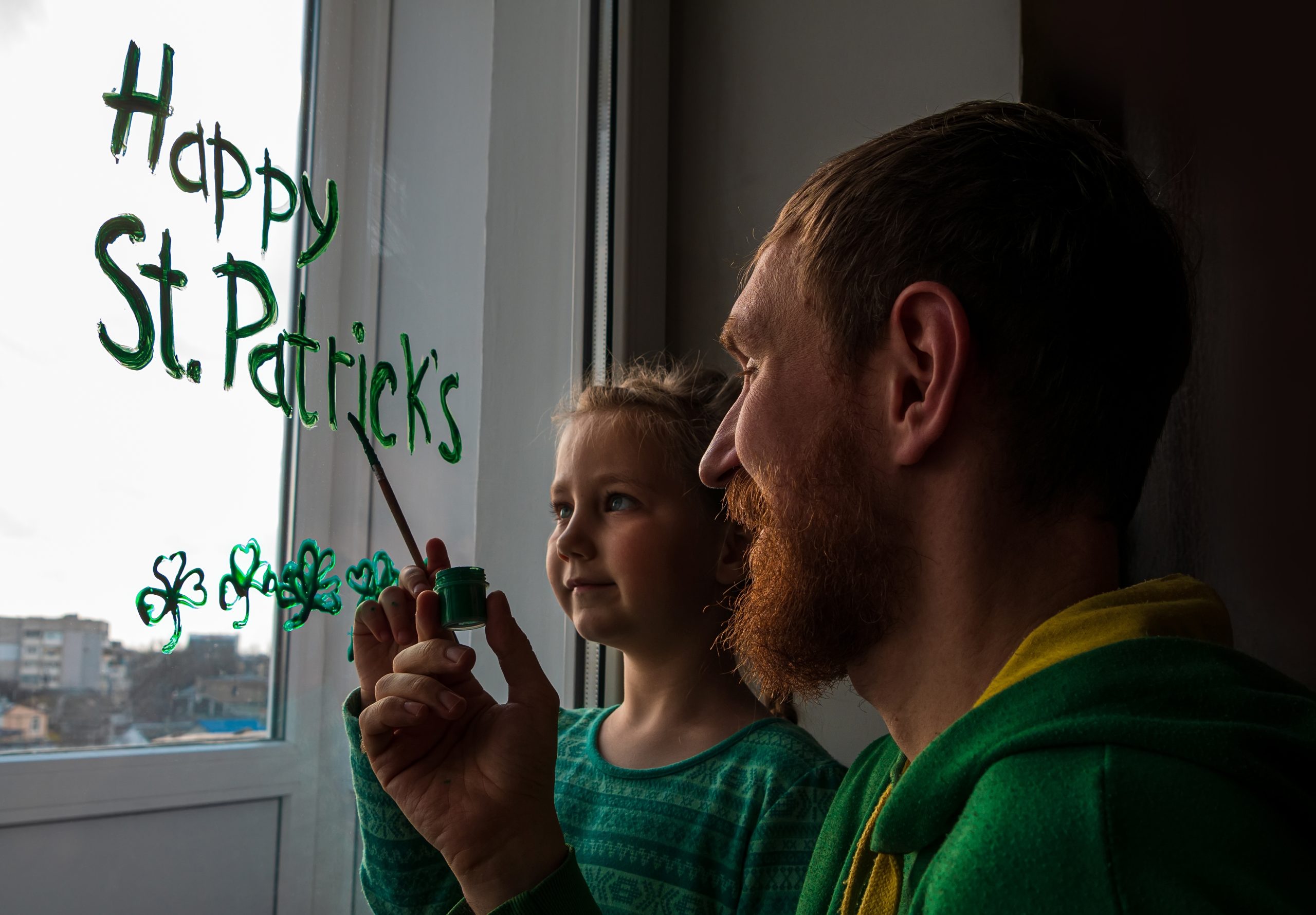 a man with his daughter painting "Happy St. Patrick's Day" on the window, as he is celebrating a sober St. Patrick's Day