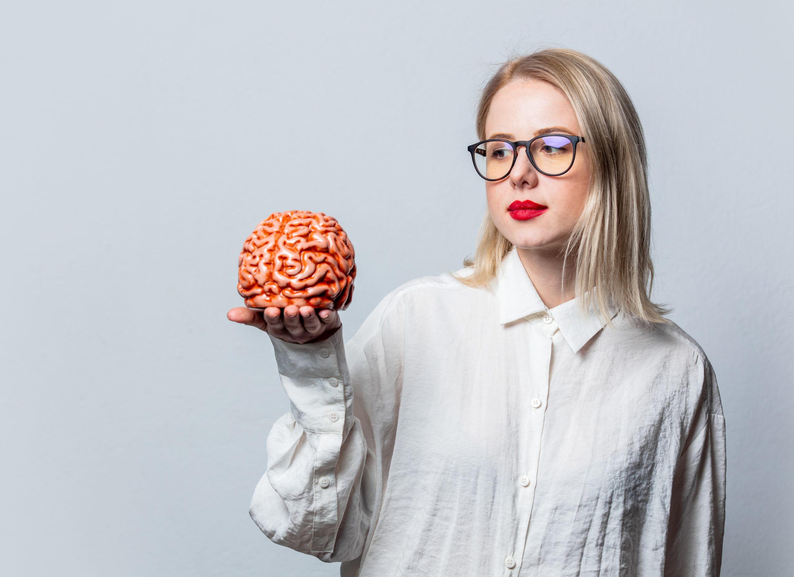 a blonde woman in a white shirt holding a human brain, highlighting the correlation between intelligence and addiction