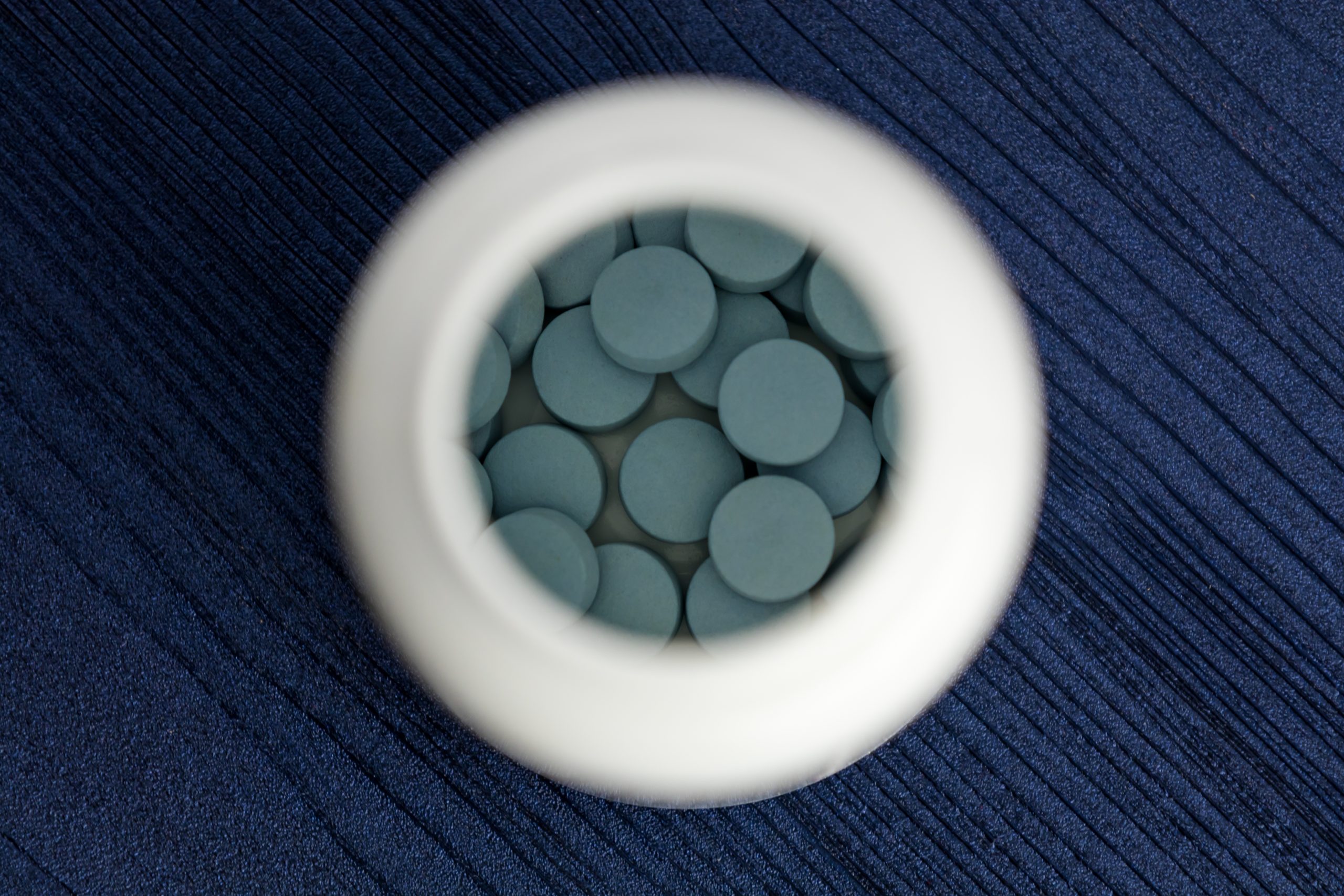 looking down into a white pill bottle with blue tablets, symbolizing klonopin side affects