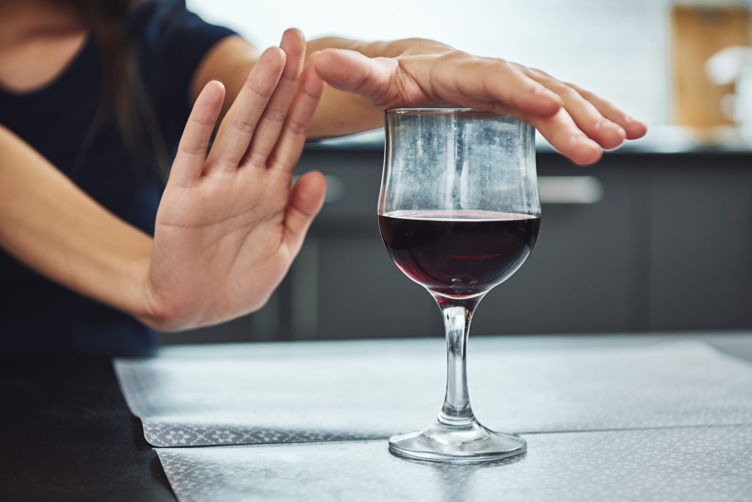 a woman refusing to drink a glass of wine of the table, highlighting the benefits of being sober