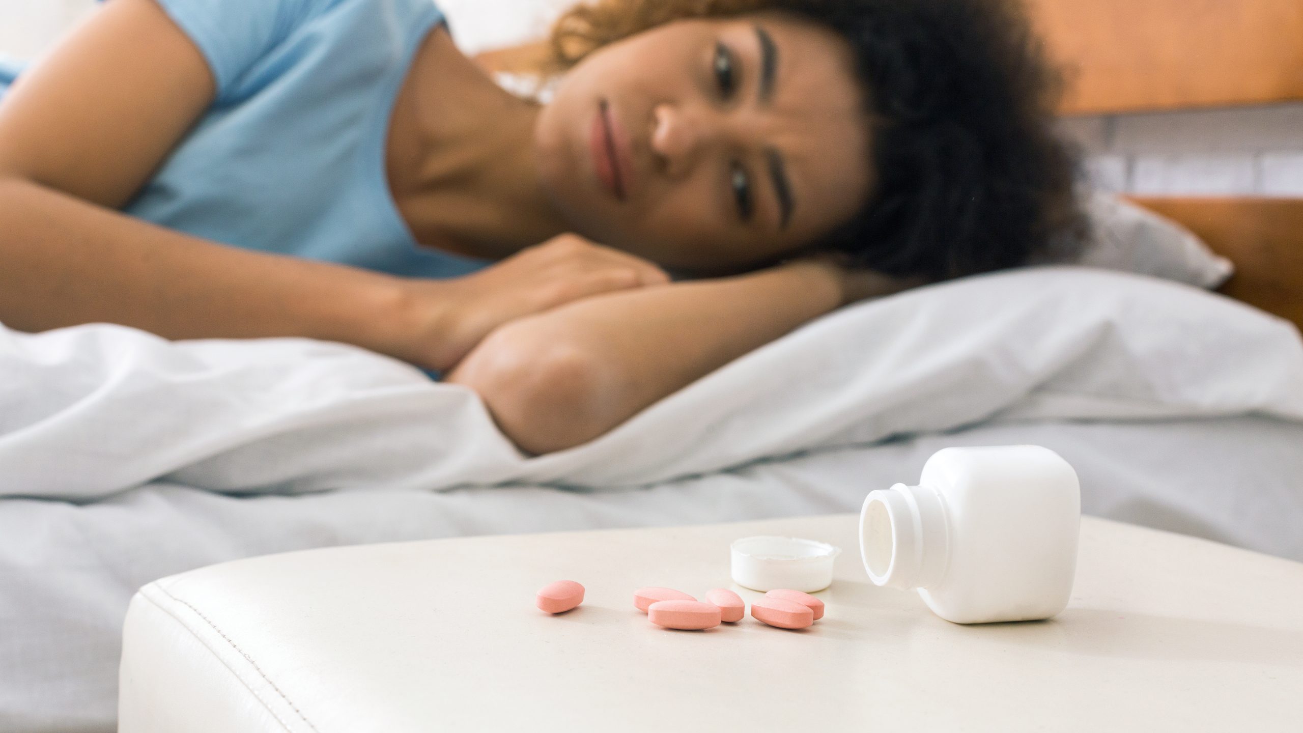 a woman lying in bed looking at sleeping pills on the nightstand, worried about sleeping pill overdose