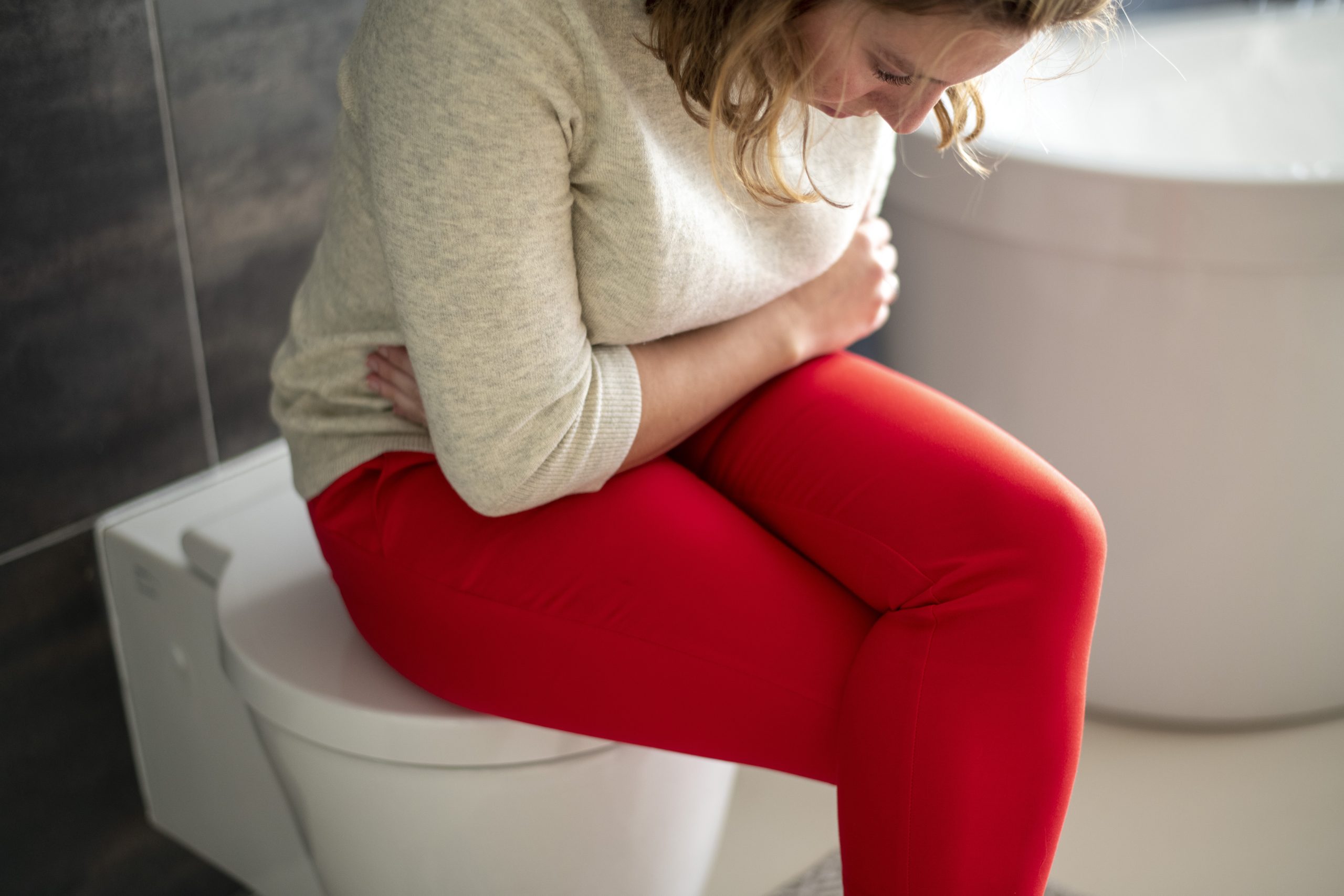 a woman sitting on the toilet lid holding her abdomen as a sign of alcohol and urinary infection