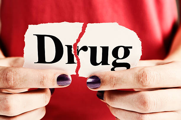 a woman tearing a piece of paper with the word "drug" written on it, attempting to break the addiction stigma during National Recovery Month