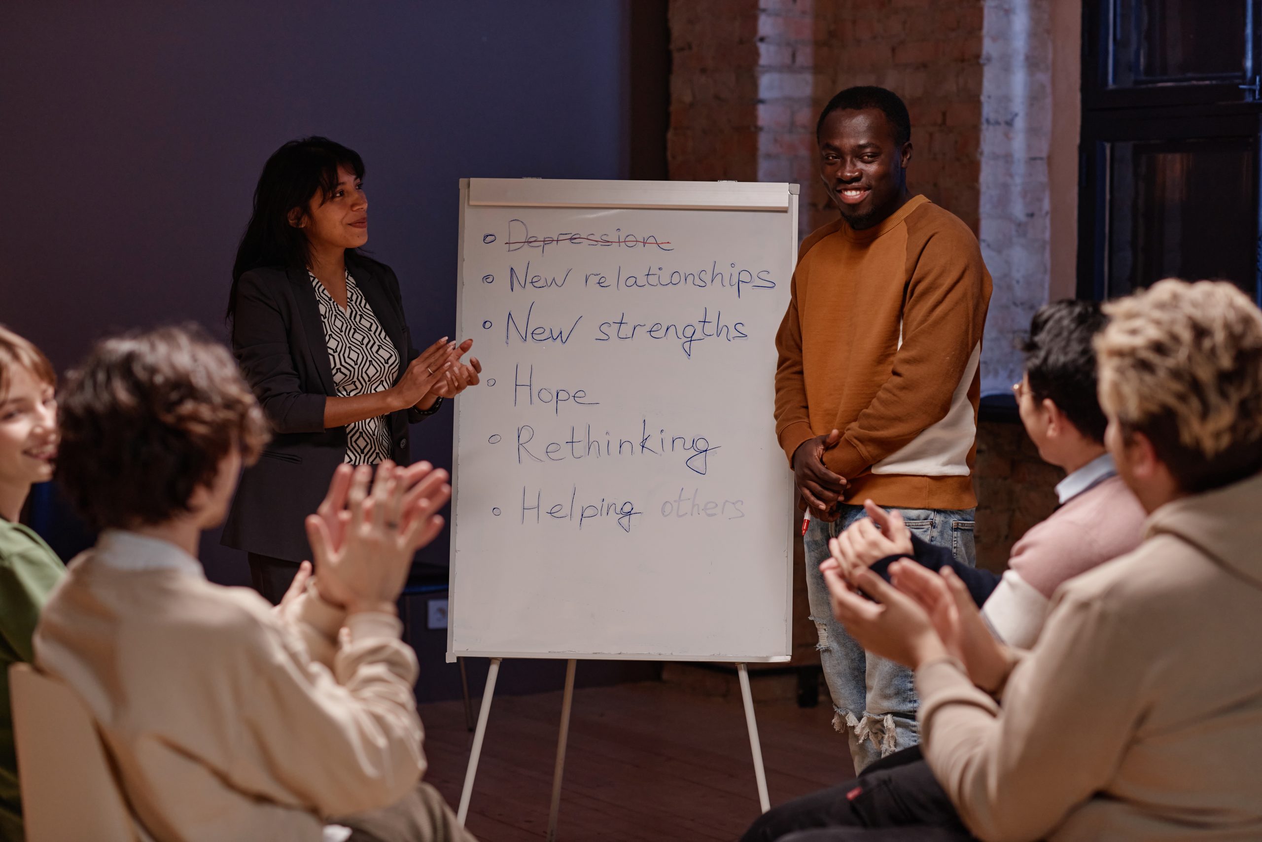 people clapping for a man who is standing next to a board with things of what to say to someone in rehab